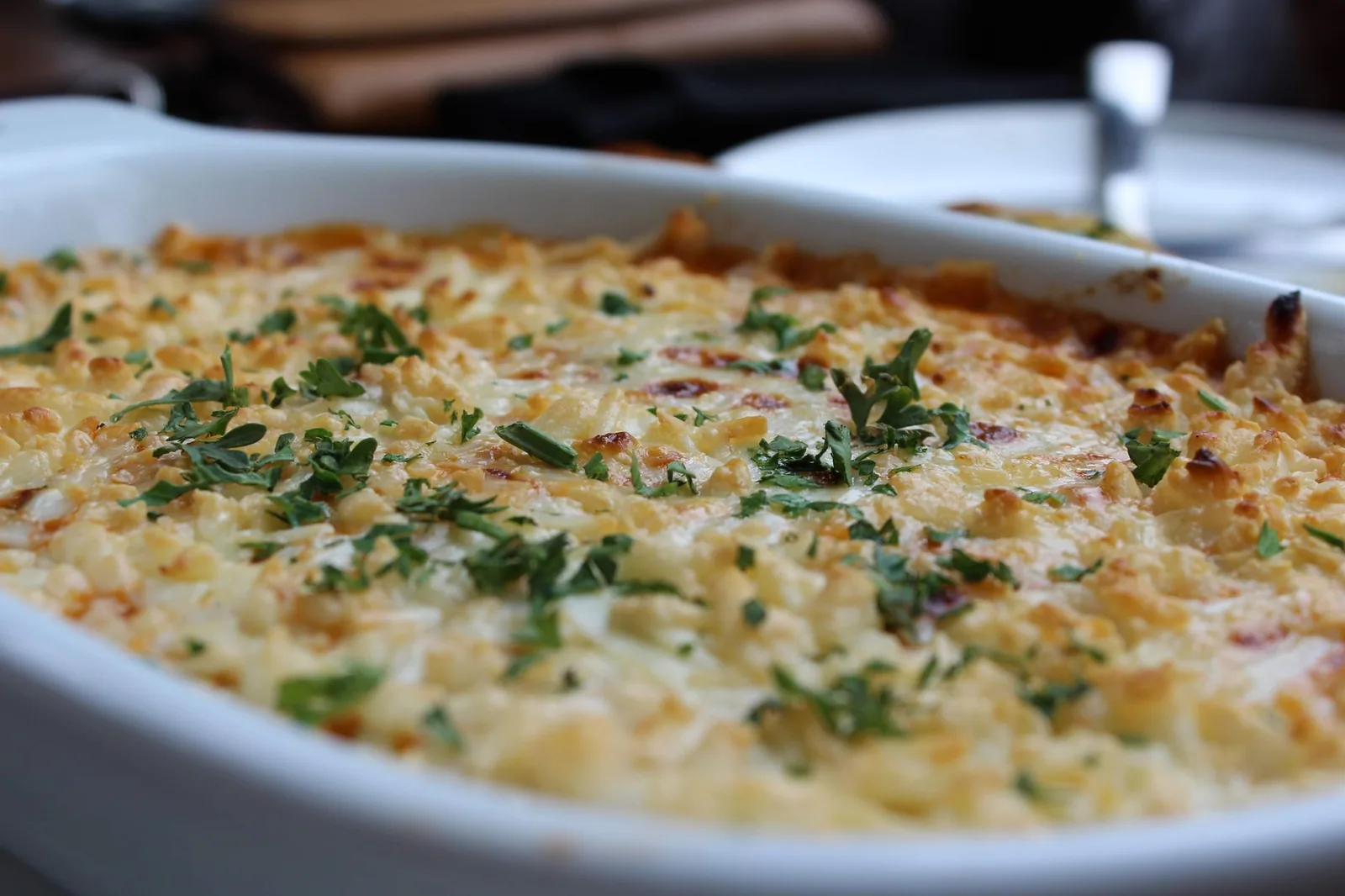 Plat à gratin ovale sortant du four, couche de béchamel gratinée et dorée parsemée de persil, comme un pastitsio grec