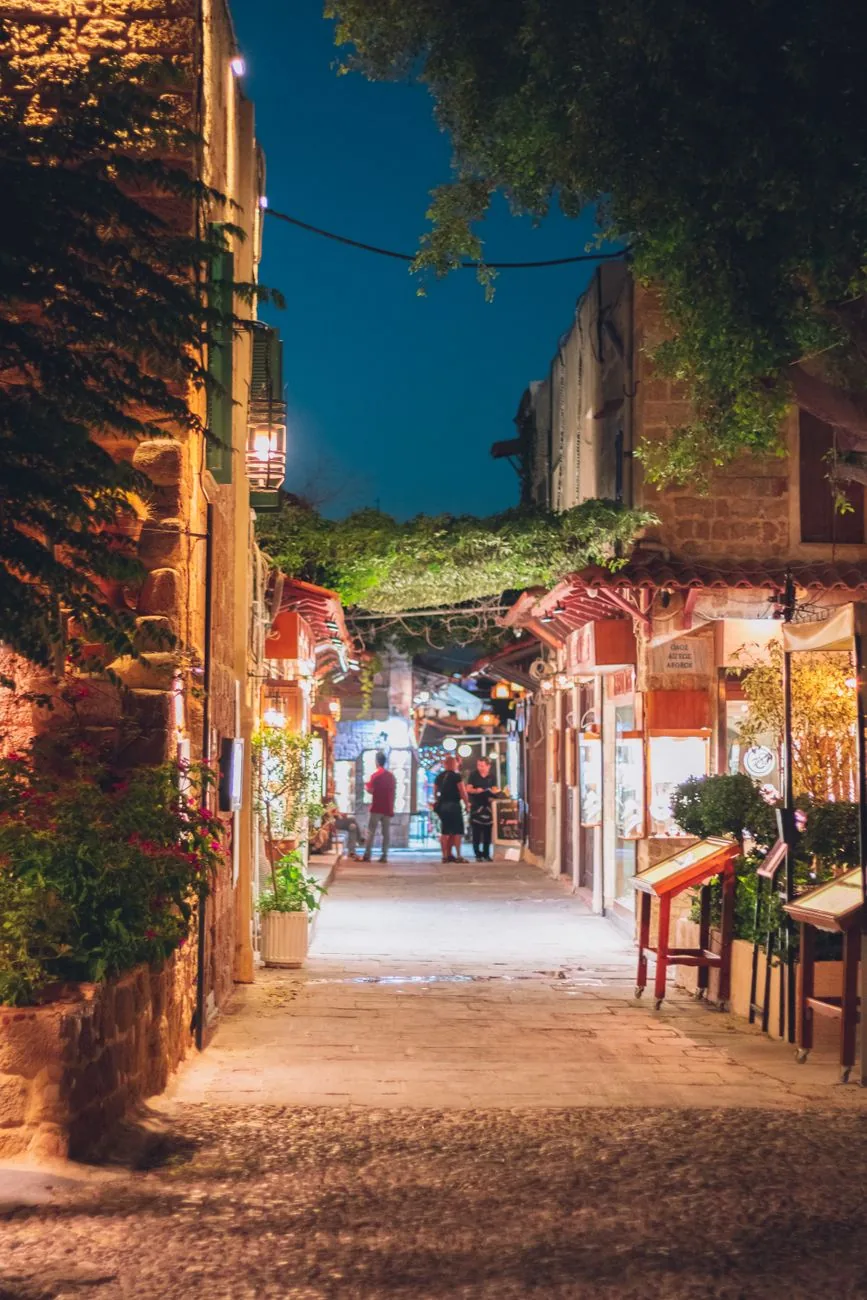 Ruelle pavée de la vieille ville médiévale de Rhodes illuminée le soir, bordée de maisons de pierre