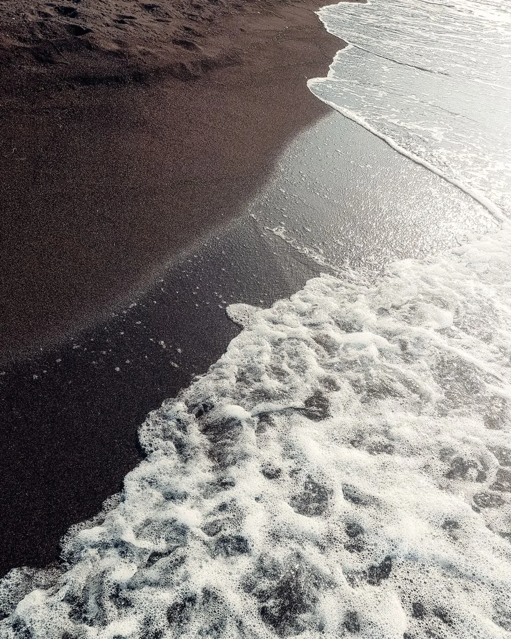 Vague sur le sable noir volcanique d'une plage de Perissa à Santorin