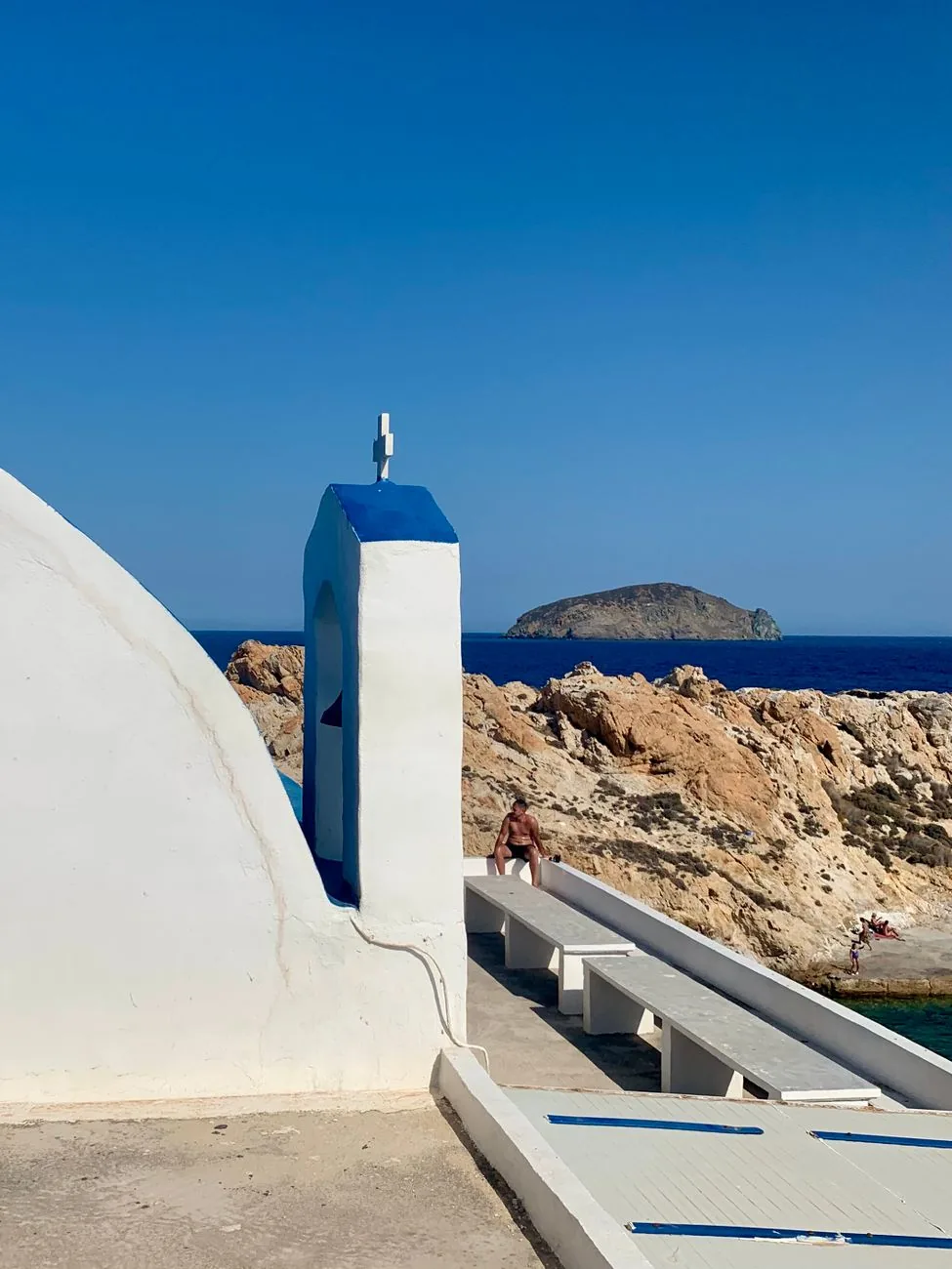 Chapelle blanche au clocher bleu posée sur les rochers de la côte de Sérifos, face à la mer et à un îlot