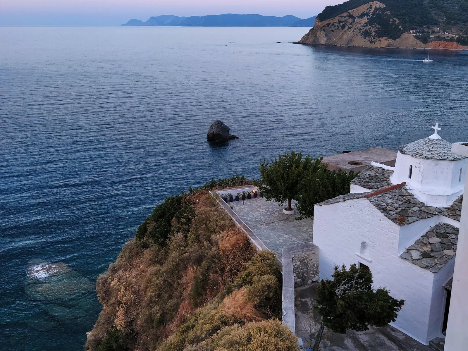 Chapelle blanche à toit de lauzes posée au bord d'une falaise de l'île de Skopelos, au dessus d'une mer calme au crépuscule