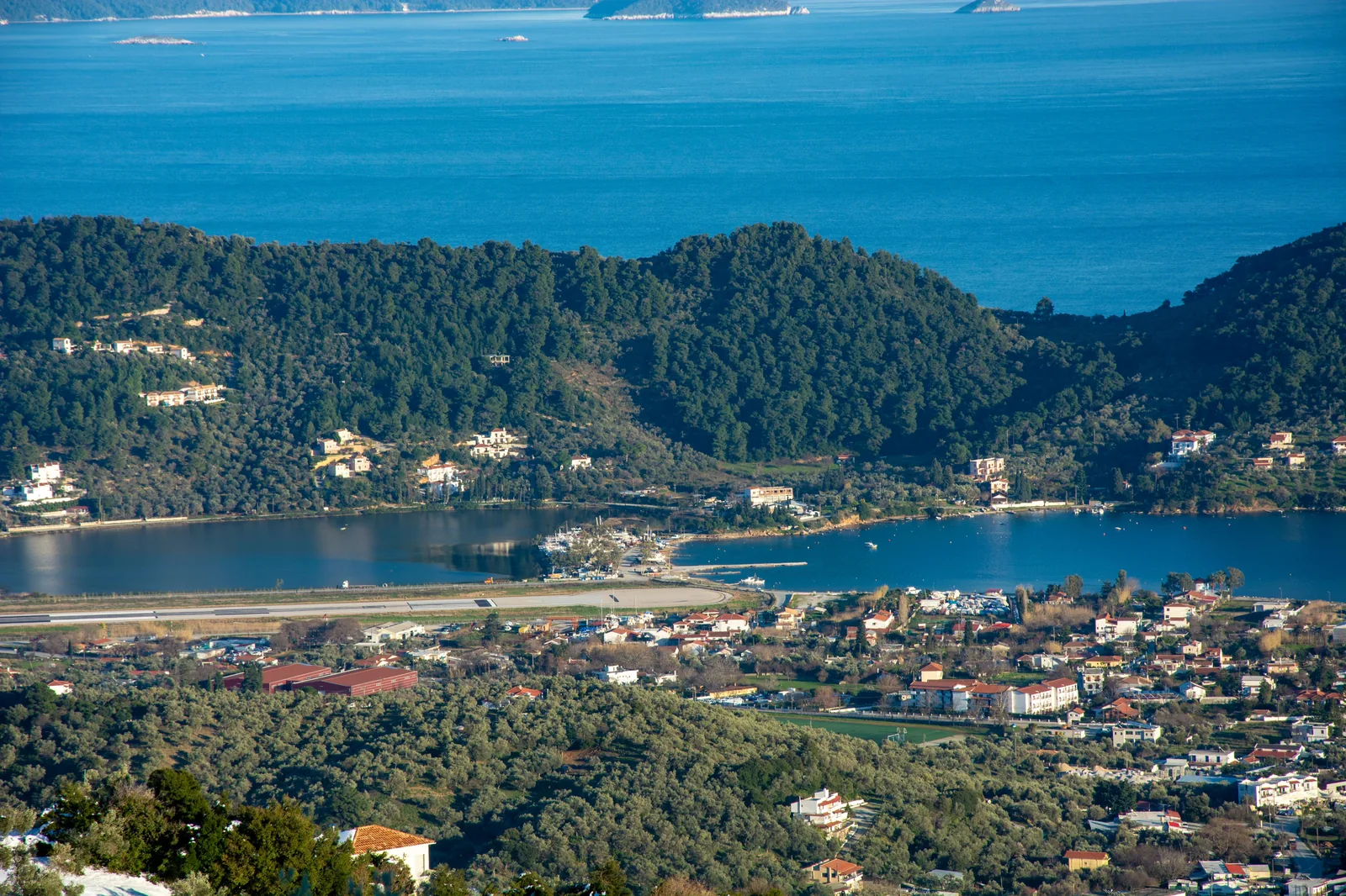 Vue aérienne de la piste de l'aéroport de Skiathos posée entre la mer et la baie intérieure, avec les collines couvertes de pins derrière