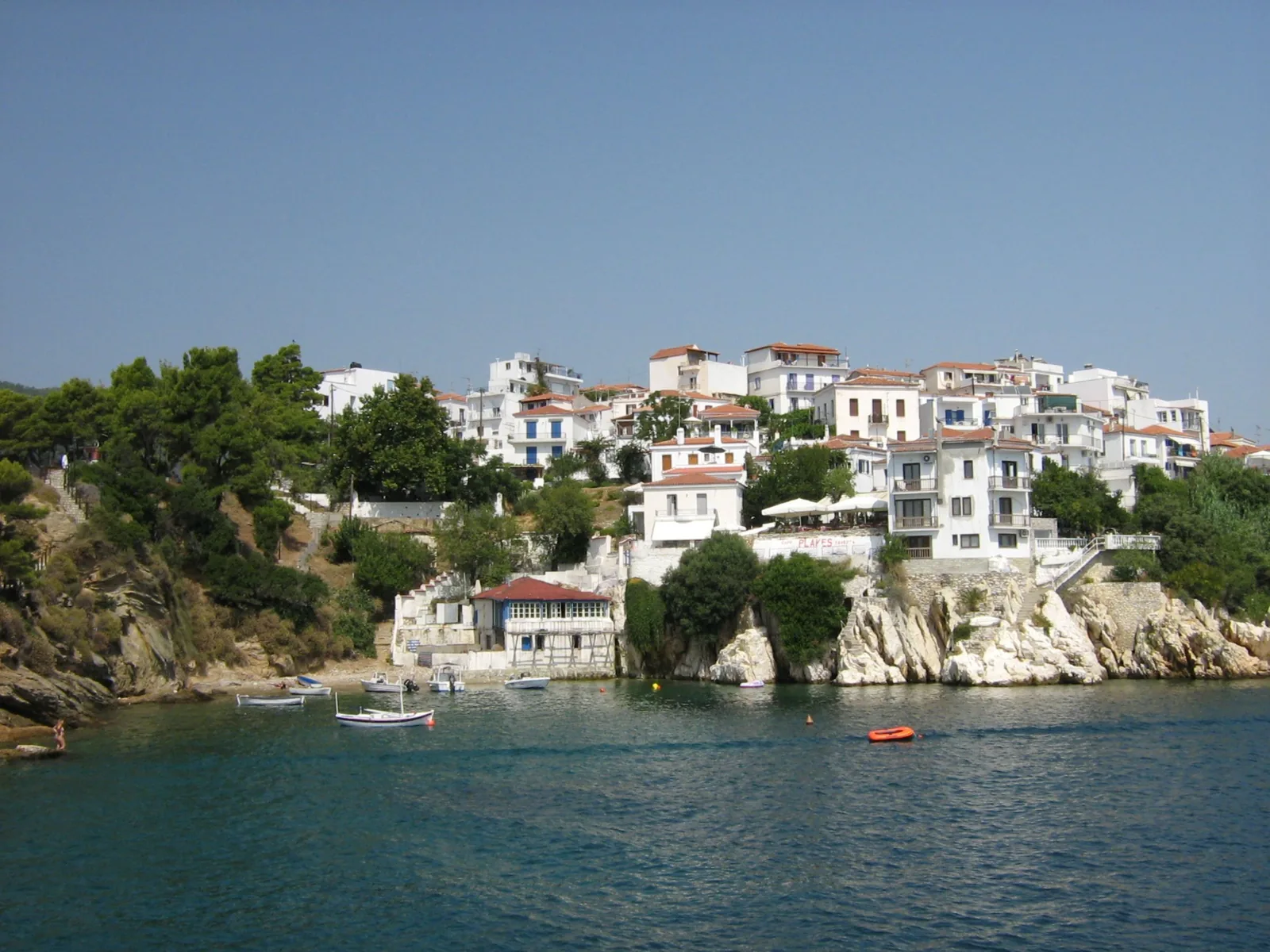 Le vieux port de Skiathos, ses maisons blanches à toits de tuiles étagées au dessus de la crique et les barques amarrées devant la presqu'île du Bourtzi