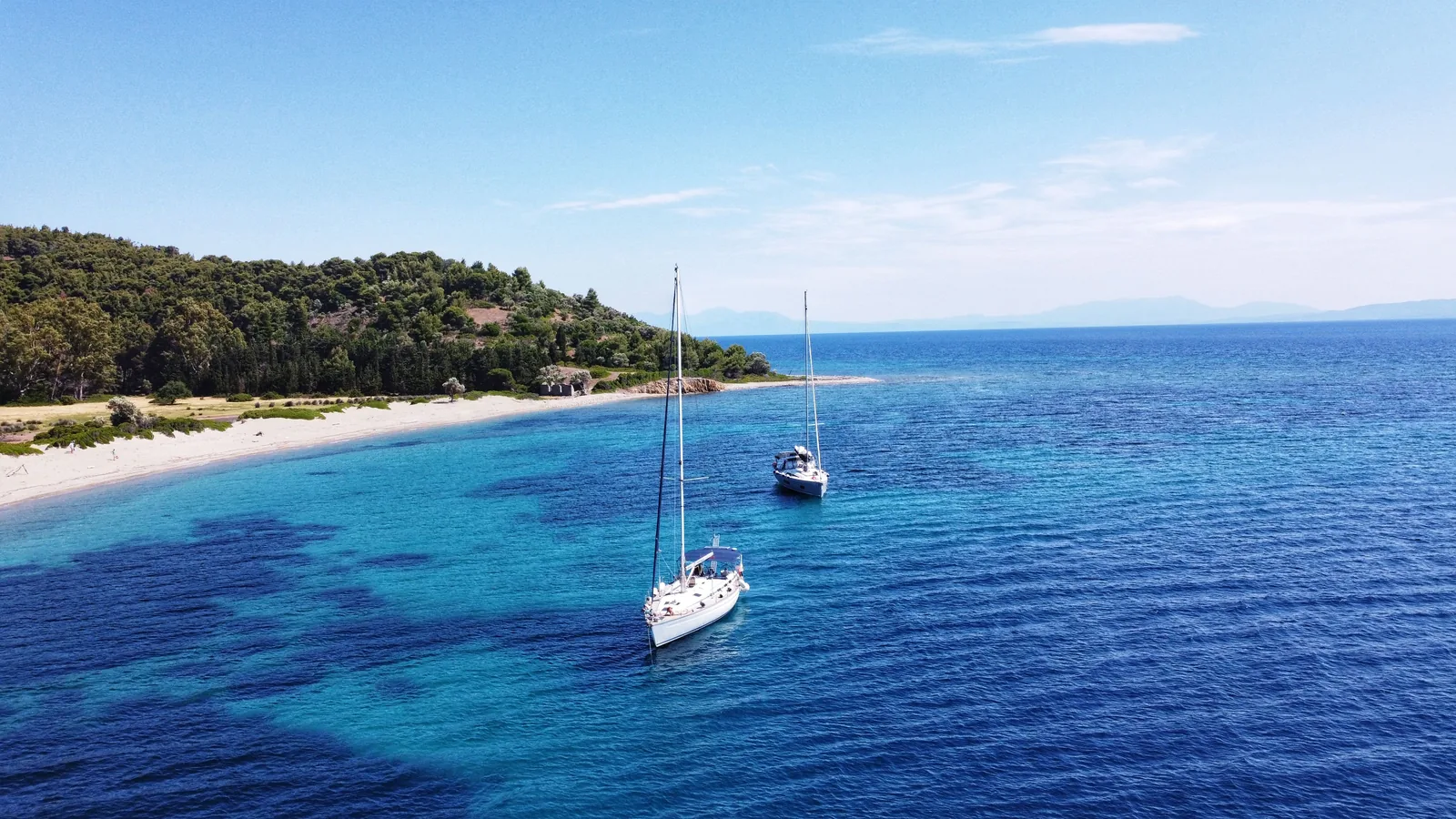 Deux voiliers au mouillage devant une plage de sable de la côte sud de Skiathos, adossée à une colline couverte de pins