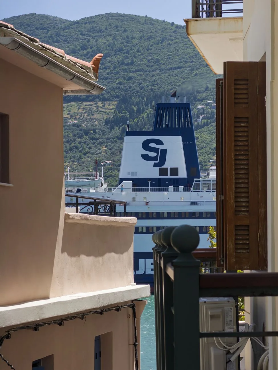 Un ferry à quai aperçu entre deux maisons de Skopelos Ville, avec les collines couvertes de pins derrière