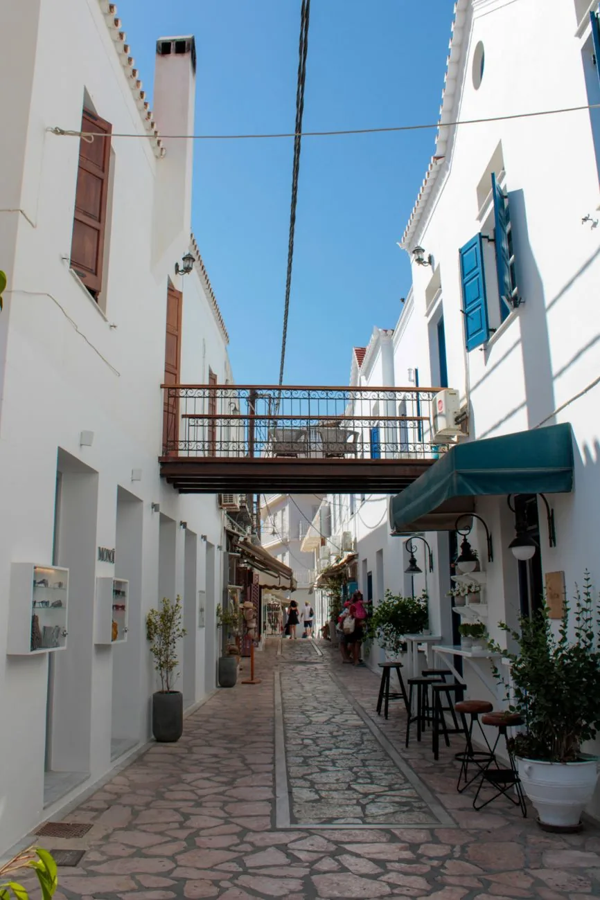 Ruelle blanche et pavée du centre de Spetses, avec ses terrasses et une passerelle entre deux maisons