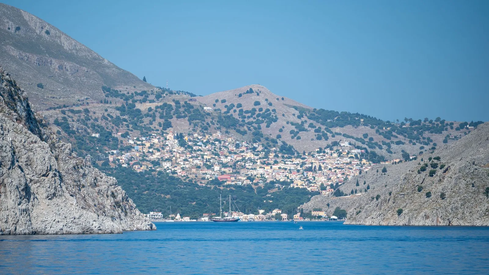 La côte rocheuse de Symi vue depuis la mer, ses versants secs et le village étagé au fond de la baie