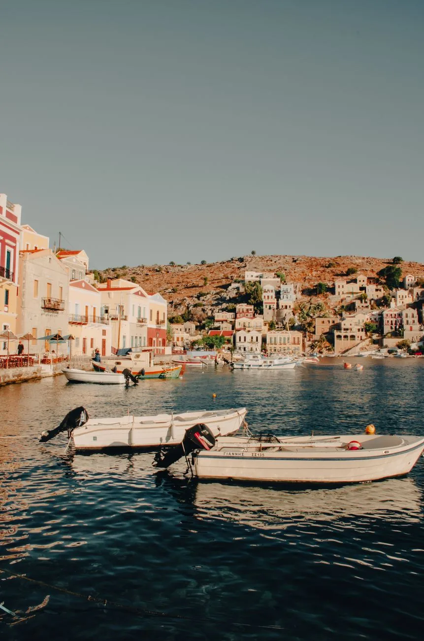 Barques amarrées dans une anse de Symi à l'eau claire, devant les maisons colorées du bord de mer