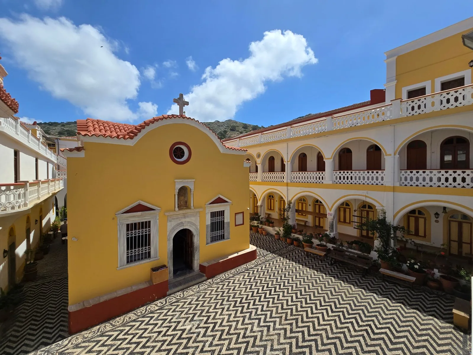 La cour du monastère de Panormitis à Symi, pavée de galets noirs et blancs en chevrons, devant l'église jaune et les bâtiments à arcades