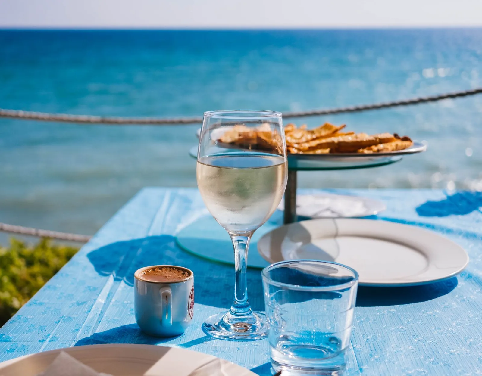 Verre de vin blanc grec sur une table de taverne à nappe bleue au bord de la mer, avec un café grec et un verre d'eau