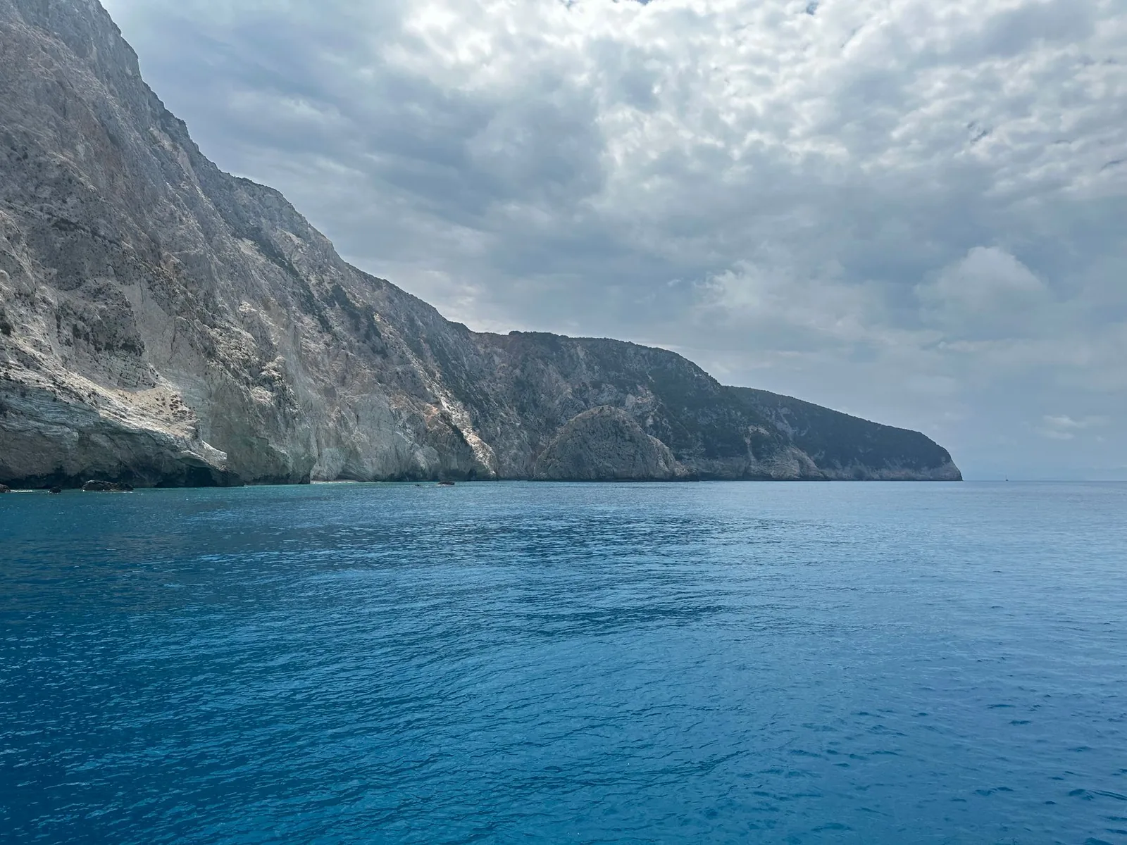 Falaise calcaire plongeant dans la mer ionienne sous un ciel couvert, sur la côte ouest de Lefkada