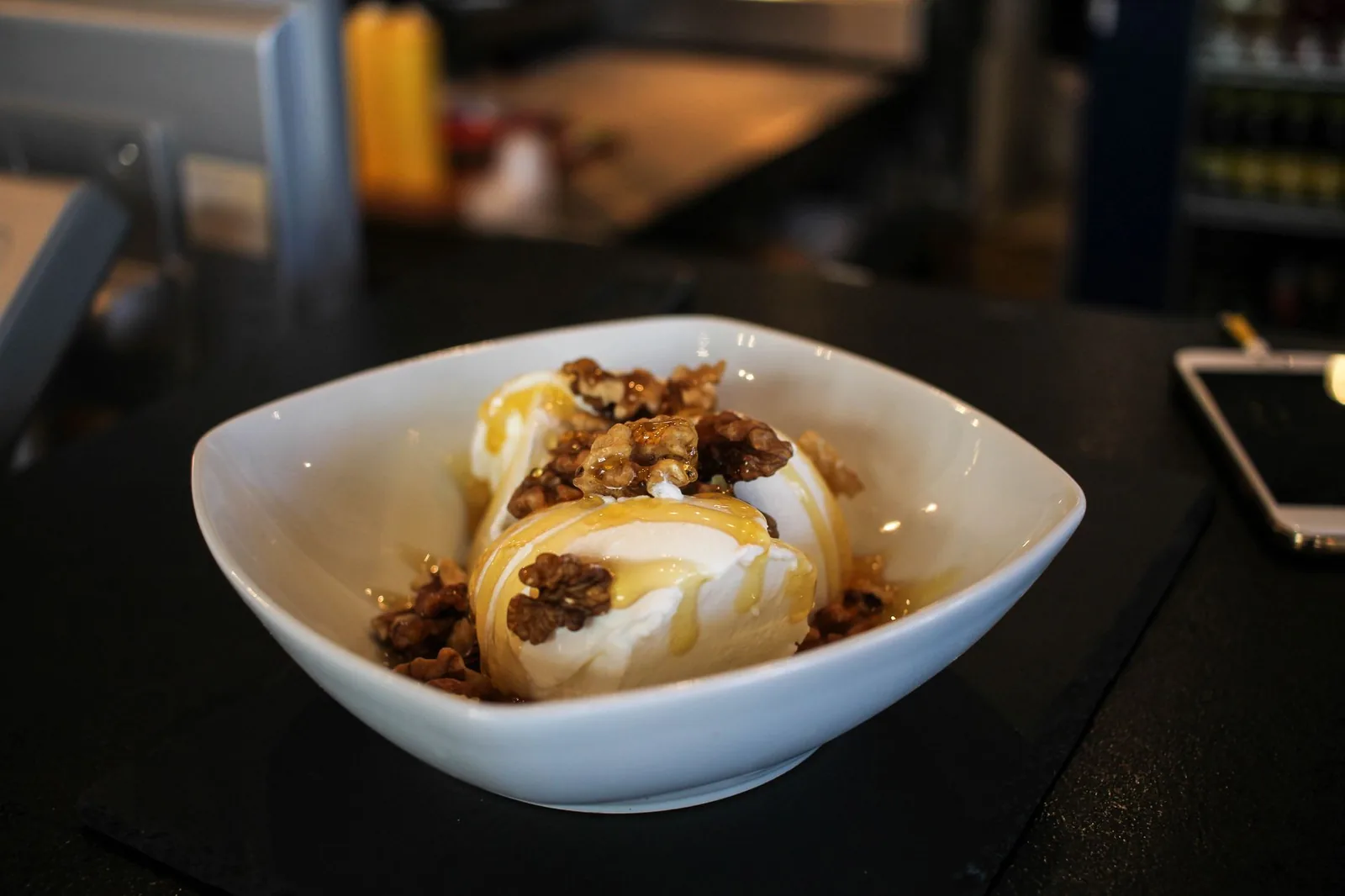Yaourt grec égoutté servi en dessert dans une coupelle blanche, nappé de miel et de noix concassées, sur un comptoir de taverne